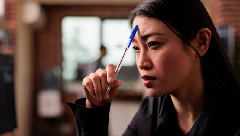 Kobieta w skupieniu z długopisem przy czole, symbolizująca poprawę pamięci i koncentracji – wsparcie Lion’s Mane a pamięć.